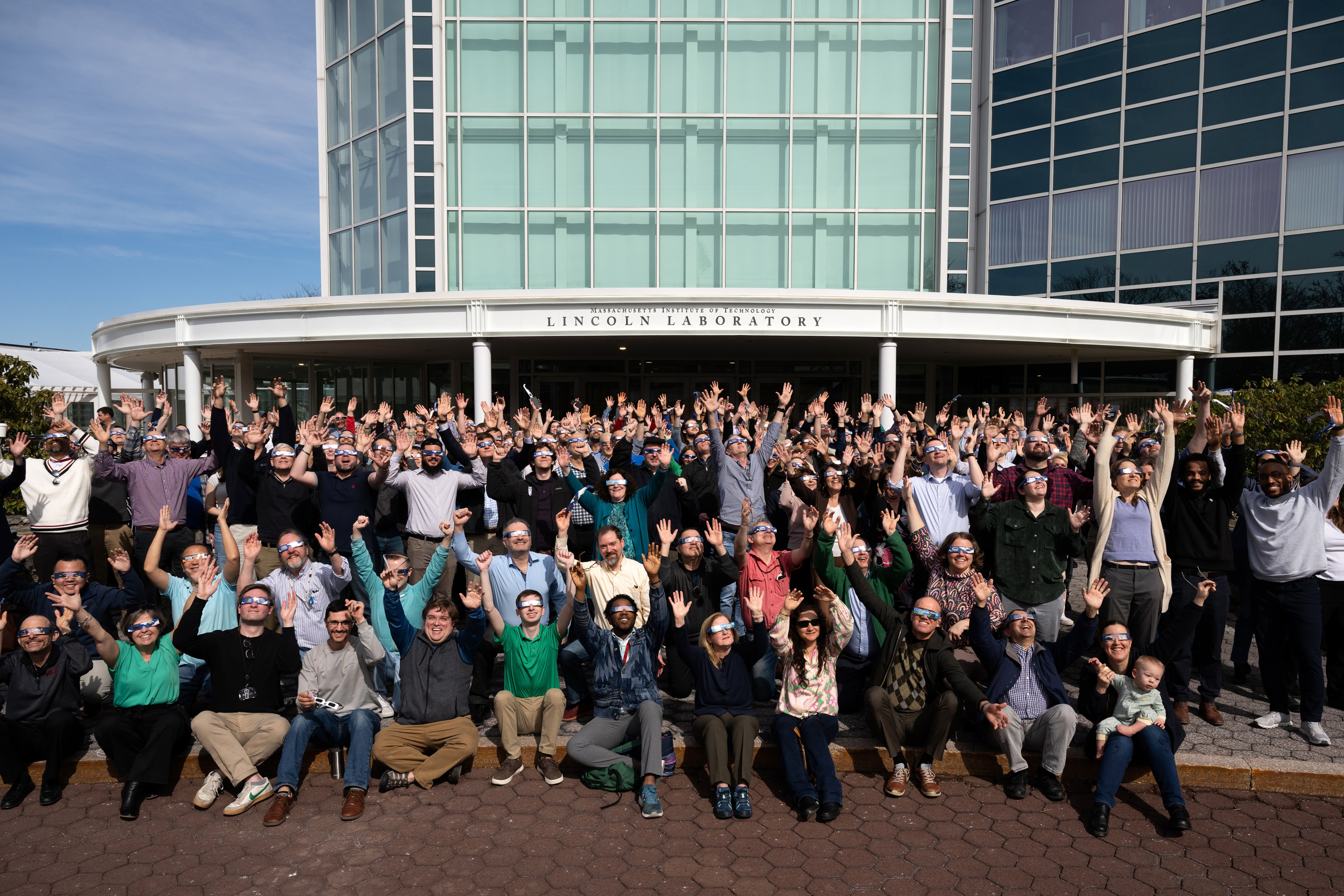 A huge crowd at the Lincoln Laboratory poses for group photo, hands up in there.