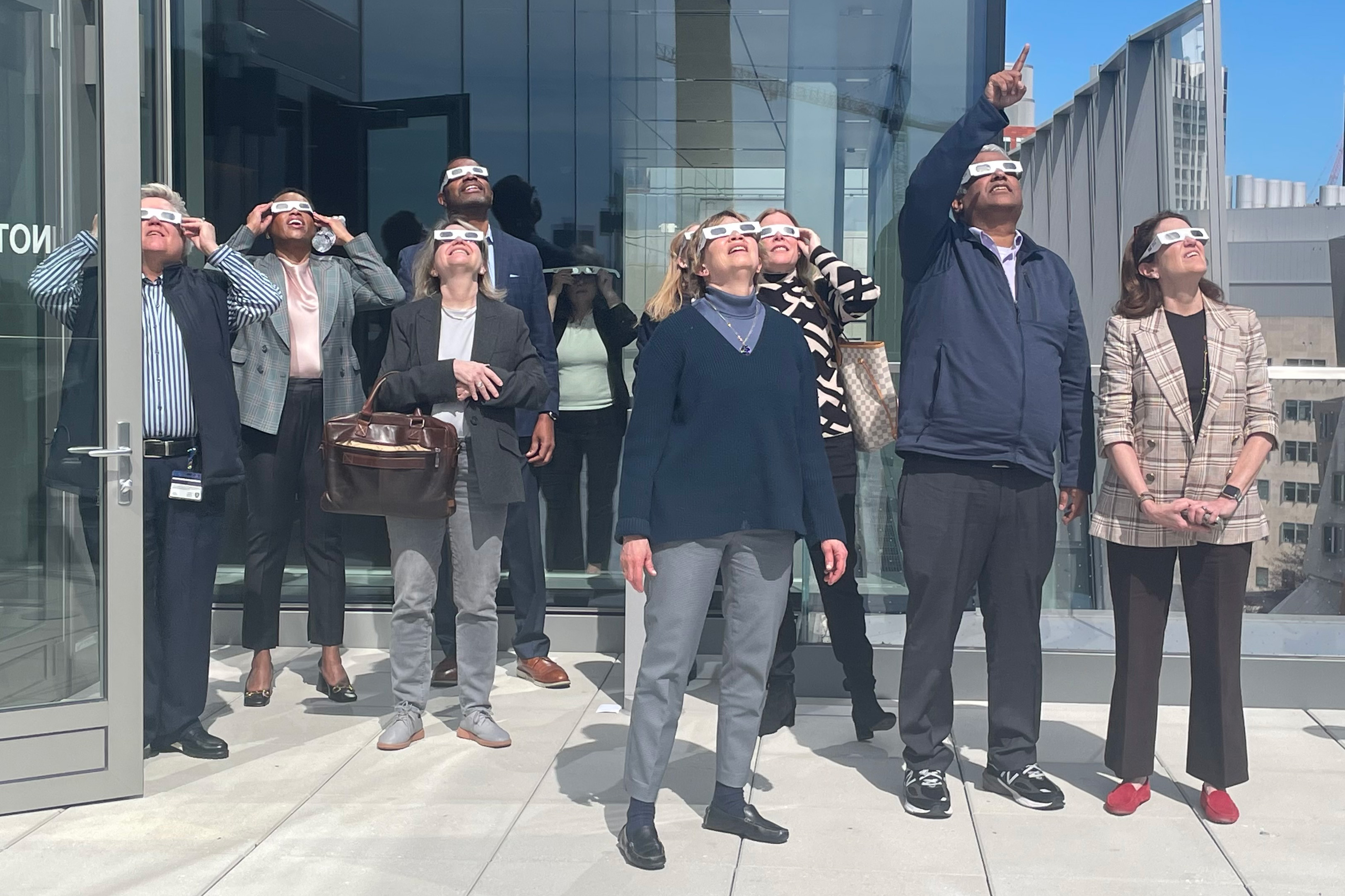 A group of MIT members, including President Sally Kornbluth look up at the eclipse from a balcony.