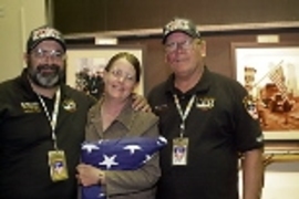 New York firefighters Mike Bellone (left) and Bob Barrett gave an American flag to Gayle Willman (center), who organized trips to Ground Zero for MIT volunteers to care for recovery workers. Behind them are photos taken at the World Trade Center disaster site.