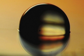Photo shows a water droplet sitting on a ferrofluid-impregnated surface, which has cloaked the droplet with a very thin layer.