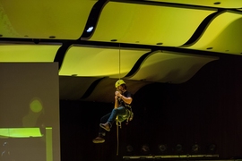A student demonstrates a rappelling device for climbers by descending from the ceiling of Kresge.
