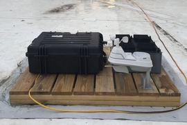 The team’s test device, which has been deployed on the roof of an MIT building for several months, was used to prove the principle behind their new energy-harvesting concept. The test device is the black box at right, behind a weather-monitoring system (white) and a set of test equipment to monitor the device’s performance (larger black case at left).

