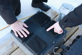 Close-up view shows the thermal resonator (black box) with its radiative cooling fins across the top. The device is filled with a phase-change material that allows it to capture energy from changing temperatures.


