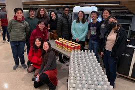 12 MIT students smile while getting water and popcorn ready in a large kitchen.