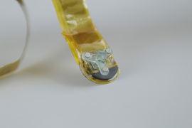A close-up of the tracker shows that it is Y-shaped and has 3 metallic discs. The tracker is at the end of a yellow strip-cable.