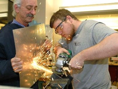Professor Woodie Flowers of mechanical engineering helps senior John Rebula work on part of a manioc grater, designed to grate large quantities of manioc or kasava for food in Haiti. The project is for 2.009, whose final presentations are Monday, Dec. 12.