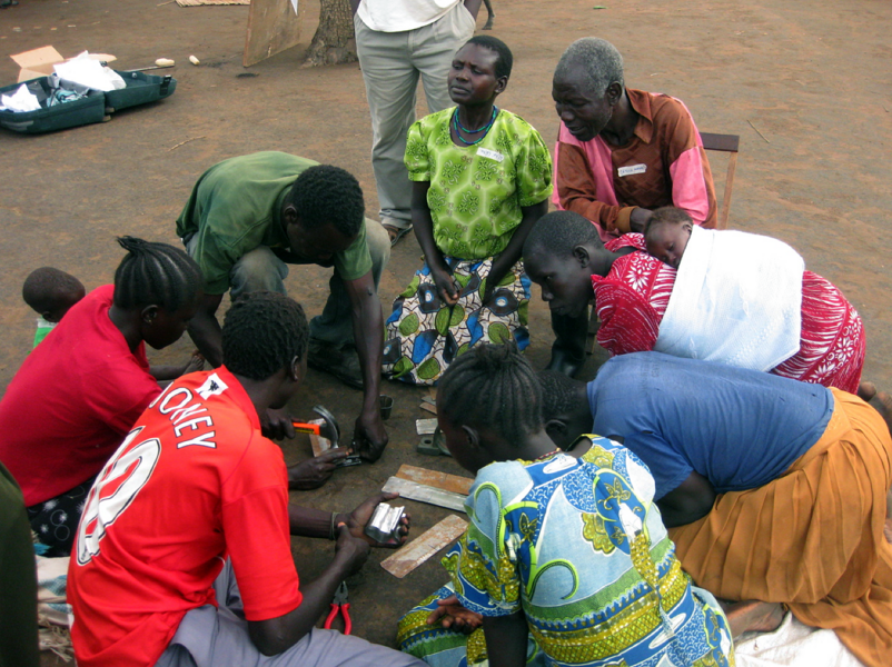 Workshop participants learn how to make corn shellers from sheet metal. Some of the women worked while carrying their babies  on their backs.