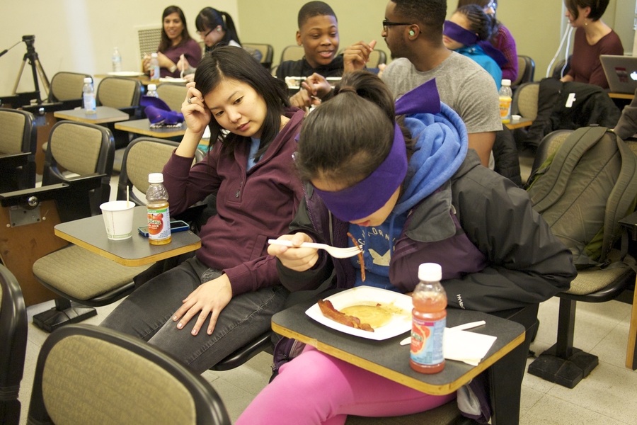 Mentor Alina Li, a junior at MIT, watches her mentee Shirley Cheung attempt to eat breakfast while blindfolded. The exercise simulated life with a nervous system disorder.