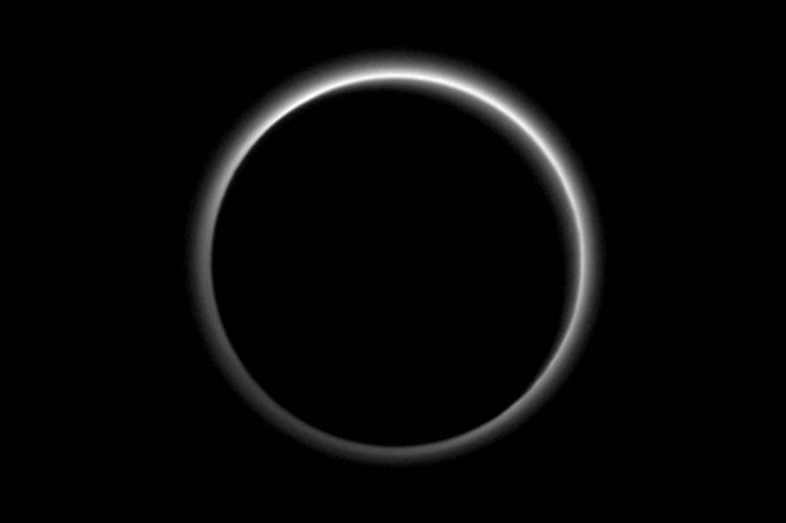 Backlit by the sun, Pluto’s atmosphere rings its silhouette like a luminous halo.