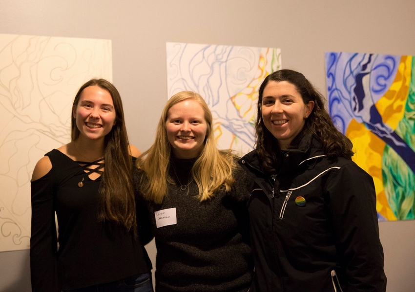 Senior Larkin Sayre (left) poses with friends in front of her paintings at the OpenMind::OpenArt gallery opening.