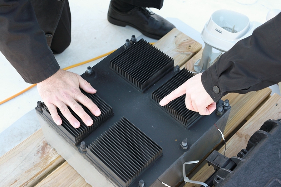 Close-up view shows the thermal resonator (black box) with its radiative cooling fins across the top. The device is filled with a phase-change material that allows it to capture energy from changing temperatures.
