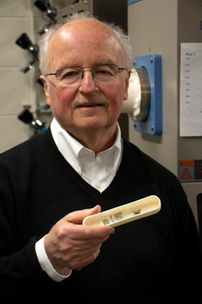 Standing in front of a high-temperature furnace for processing electroceramic materials, MIT Professor Harry Tuller holds several samples of metalized thin film metal oxides used in gas sensors, fuel cells, and catalytic converters.