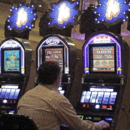 A person sits in front of slot machine with back turned to camera.