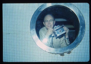 Harold “Doc” Edgerton holds a Polariod camera while photographed from inside the MIT pool.