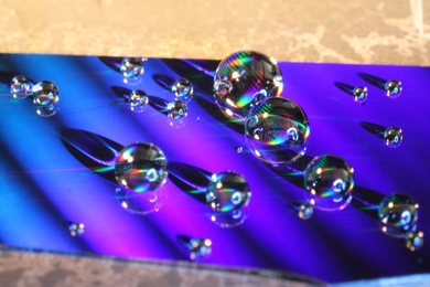 This photo shows water droplets placed on the nanostructured surface developed by MIT researchers. The colors are caused by diffraction of visible light from the tiny structures on the surface, ridges with a specially designed shape. 