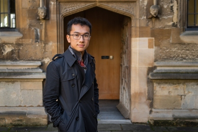 Sihao Huang poses for a photo standing outside a weathered stone doorway with intricate carvings on the exterior