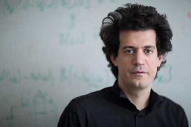 Headshot photo of Costis Daskalakis in front of a whiteboard
