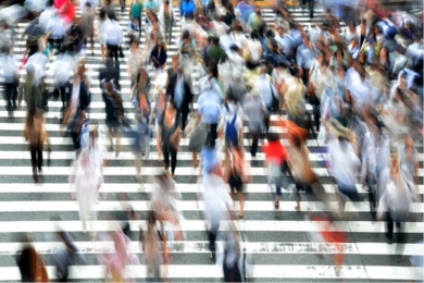 Photo of a crowd walking through a crosswalk. The people are motion-blurred.
