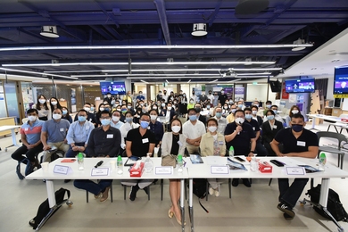 Approximately 60 people, all wearing masks, pose for a group photo inside a large open office space