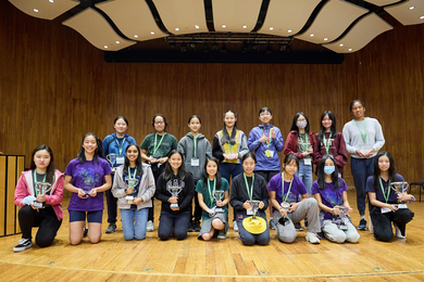 17 girls pose with their trophies on a stage at MIT