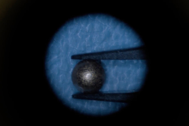 A tiny spherical magnet is held between tweezers in a microscopic photo.