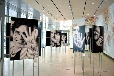 Several grayscale photographs of scientists on stands in a gallery. Each scientist is holding up one hand with words or scientific symbols written on it.
