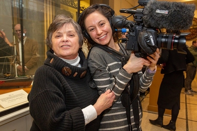 Photo of Leslie Regan hugging a student carrying a large camera