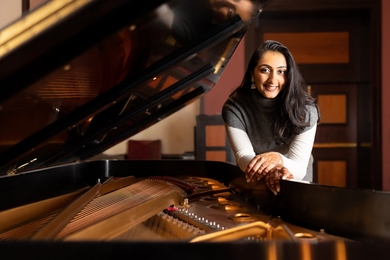 Ananya Gurumurthy leaning on an open piano and smiling