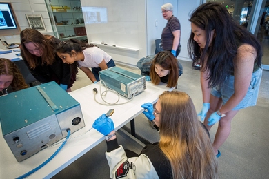 6 students surround a vintage cardiac arrhythmia detector, examining it closely.