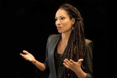 Photo of Ruha Benjamin speaking and gesturing with her hands against a black background