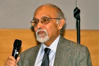 Closeup of Sanjoy Mitter, an older gentleman, speaking into a microphone in an indoor space