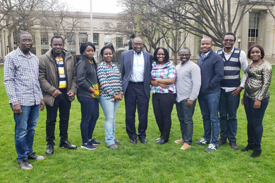 Ten Black individuals pose together in a line on a spring day on the grass at Killian Court in front of the MIT Dome.
