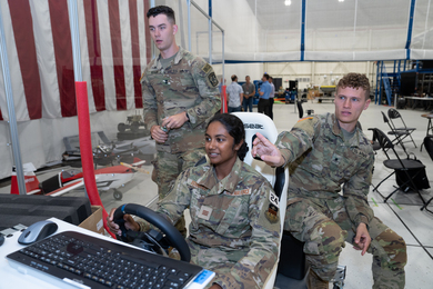 Three cadets are pictured. One is seated, operating a steering wheel that controls a robot off screen. The two other cadets look at the off-screen display.