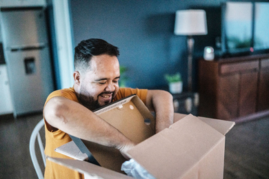 A smiling man opens up a cardboard box in his home
