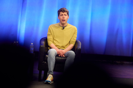 Sam Altman speaks while on stage. Blurry audience is in the foreground.