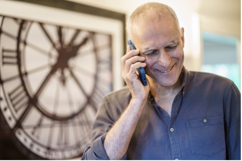 Moungi Bawendi smiles while talking on his cell phone. A framed print of a large clock is in the background.