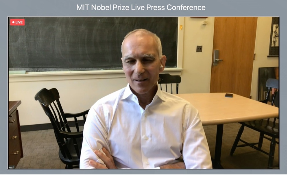 A screenshot of Moungi Bawendi speaking in the online press conference. He is seated, with a table and chalkboard behind him. At the top of the screen is the title “MIT Nobel Prize Live Press Conference.” 