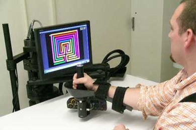 A patient uses a robotic therapy device invented at MIT. The robotic joystick guides the patient’s arm as he tries to move the robot handle toward a moving or stationary target shown on the computer monitor. If the person starts moving in the wrong direction or does not move, the robotic arm gently nudges his arm in the right direction.