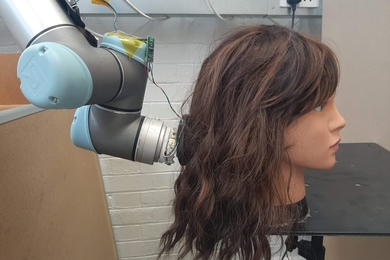 Photo of a robotic arm brushing a manequin's long, brown hair