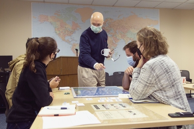 Photo of Eric Heginbotham, masked, standing at a table with MIT students sitting around it