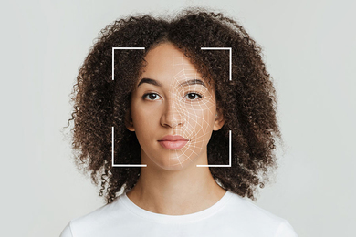 Photo of a woman in front of a white background with a cropped square outline focused on her face and small triangles marking the contours of her skin, indicating she is being scanned by a camera