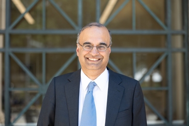 Portrait photo of Deepto Chakrabarty standing in front of a glass window crosscut by decorative metal bars