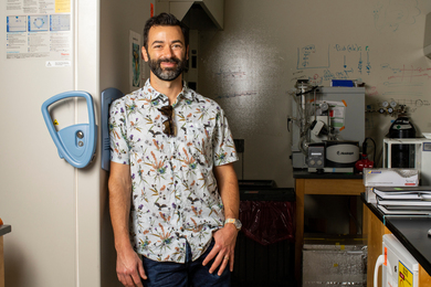 Photo of Alex Shalek standing by the wall of a science lab