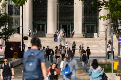 A busy scene outside MIT with pedestrians walking along a pathway and up stairs toward the Institute's main entrance.