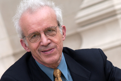 Daniel Kleppner poses, seated on stone steps with a stone column behind him