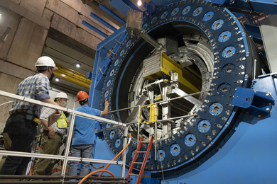 Three people inspect a gigantic blue Collider, with a circular opening.