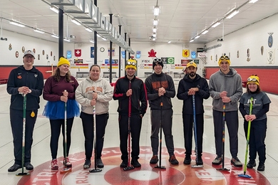 8 members of MIT's Curling team pose standing in a hockey rink.