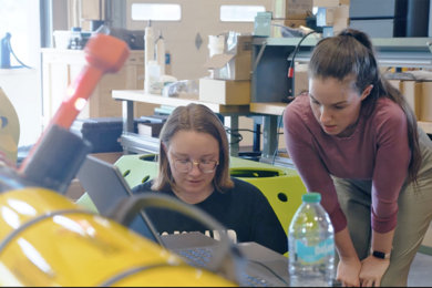 Ivy Mahncke and another individual work on a yellow autonomous vehicle in a lab