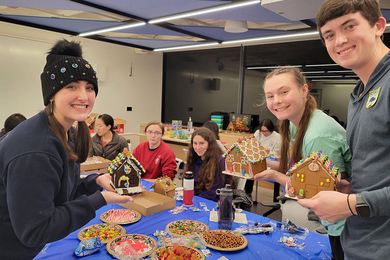 Half a dozen students show off the gingerbread houses they've just decorated