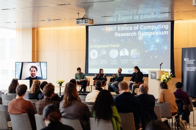 Four people have a discussion on a stage, while a fifth appears on a large monitor